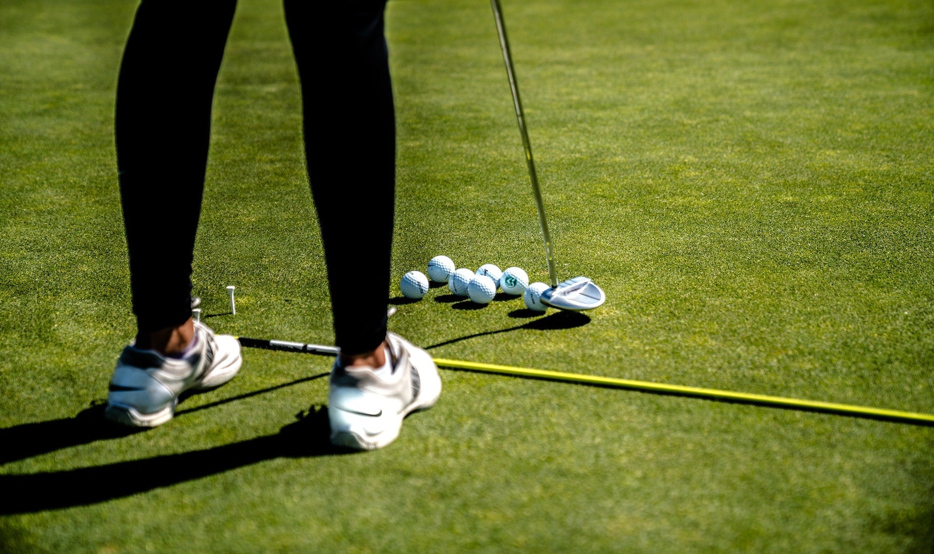 Junge weibliche Golferin, die mit einem Odyssey Putter auf dem Green steht und Golfbälle spielt.